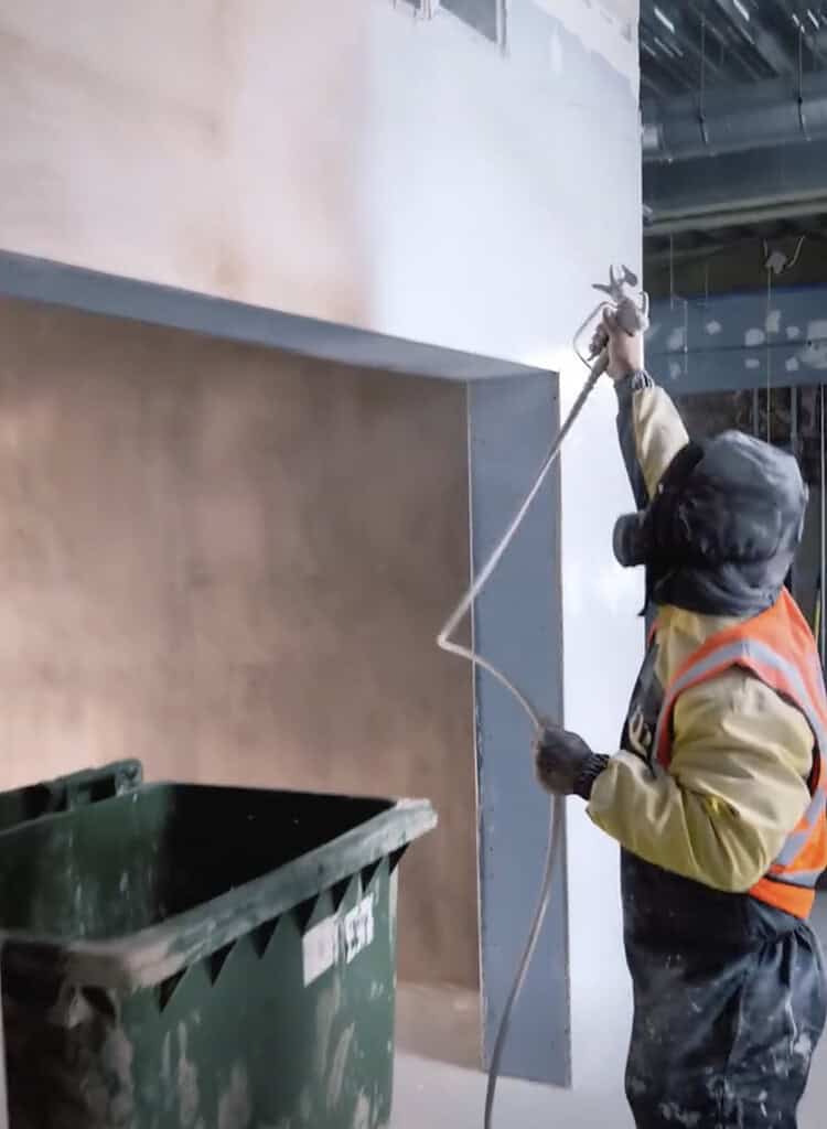 Professional decorator using airless spraying equipment to paint an exterior wall on a property in Exeter